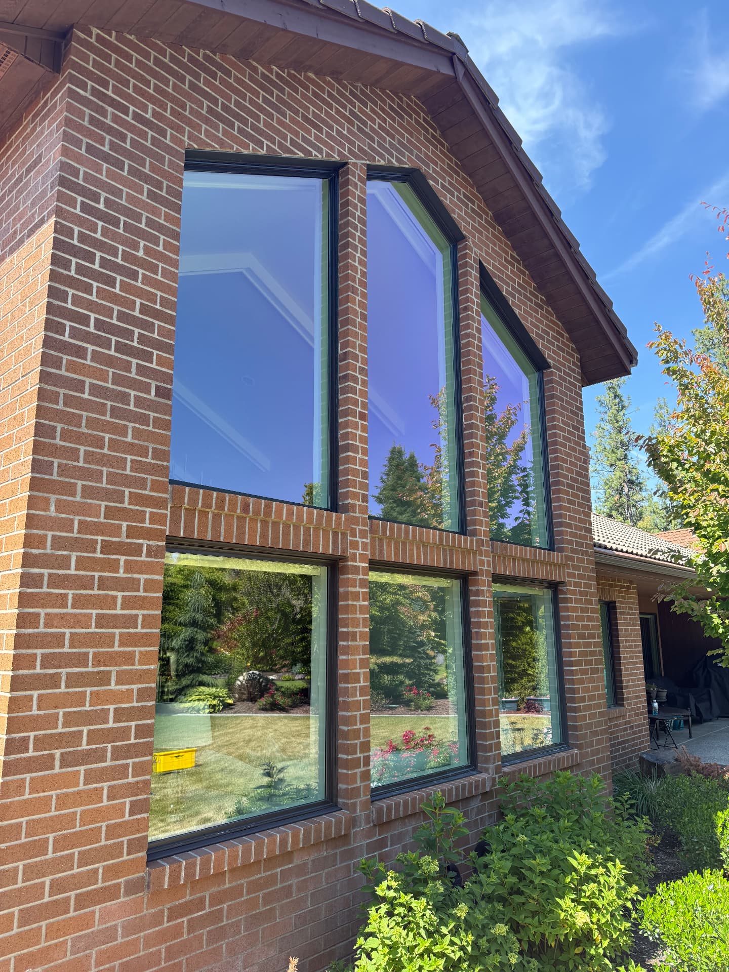 Brick home with tall picture windows reflecting a clear blue sky after cleaning